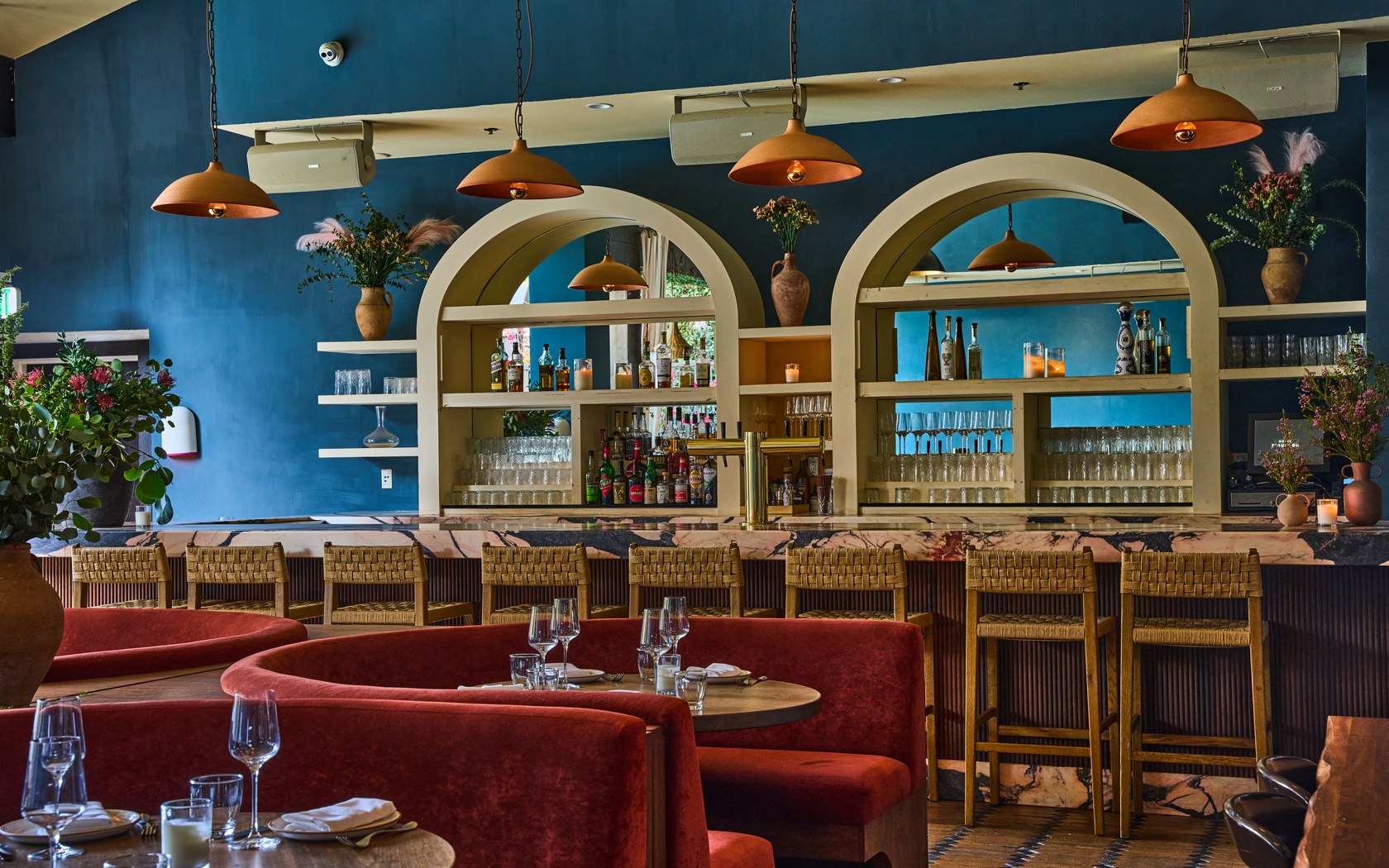 The dining room at Florence by the Water with navy walls, cream arches, and terracotta velvet booths